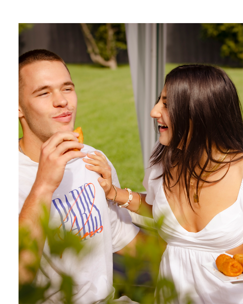 Young couple laugh and enjoy Beef Pan Rolls in sunny garden.