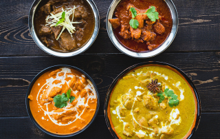 A top down image of 4 curries on a dark wooden benchtop