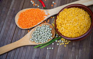 Top down image of various lentils atop wooden spoons on a wooden benchtop.