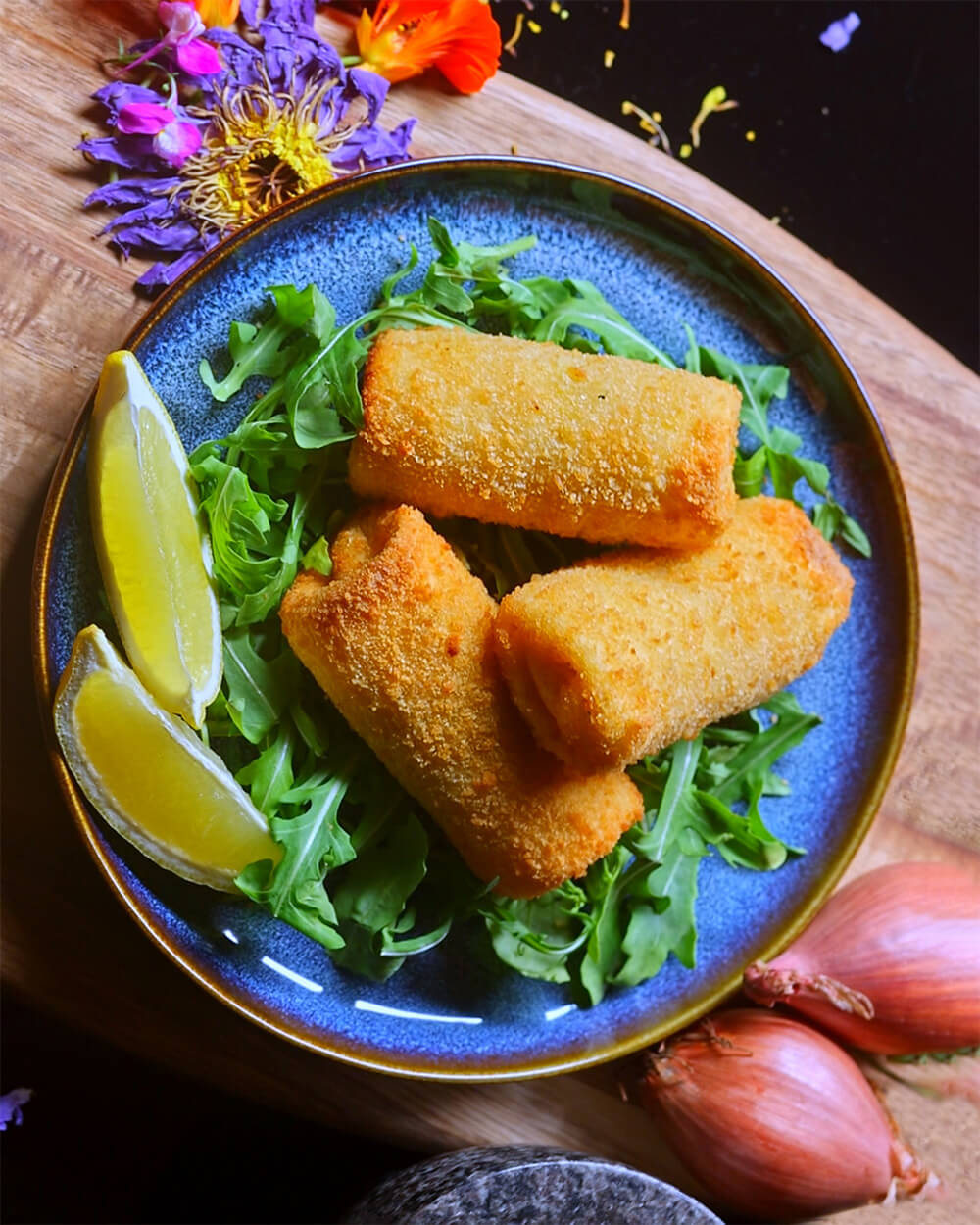 Top down image of Beef & Potato Pan Rolls with Rocket, Lemon Wedges and floral decorations.