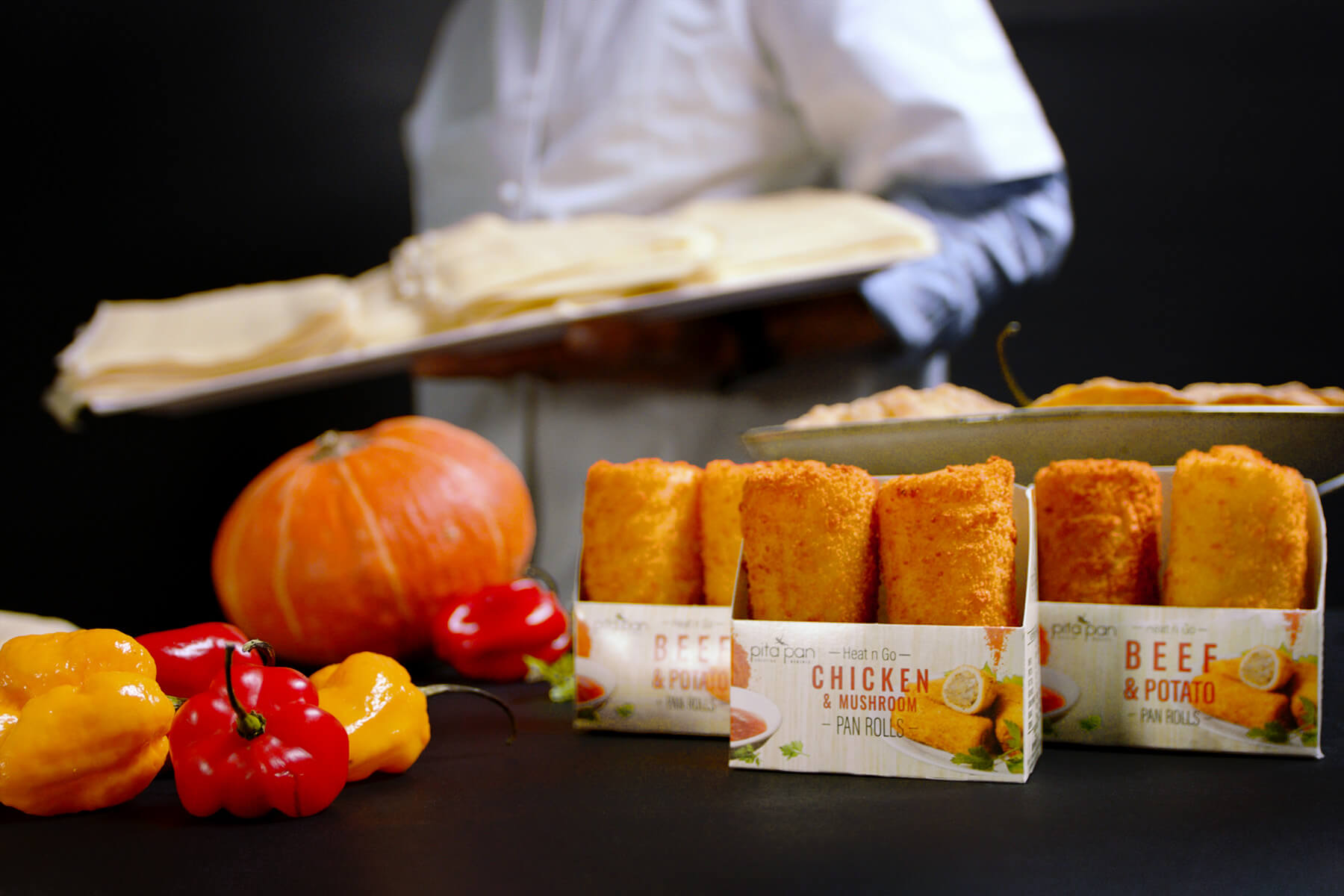 Chef walks in background out of focus behind assortment of Pan Rolls and food decorations.